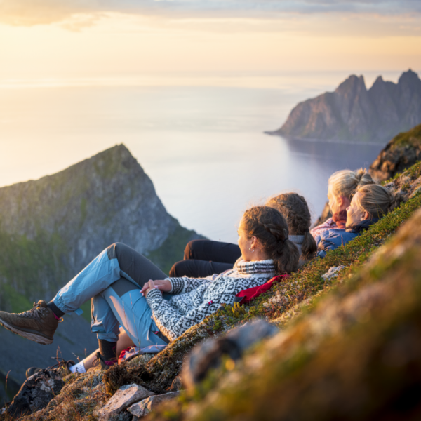 Group of friends sitting on a mountaintop enjoying the midnight sun