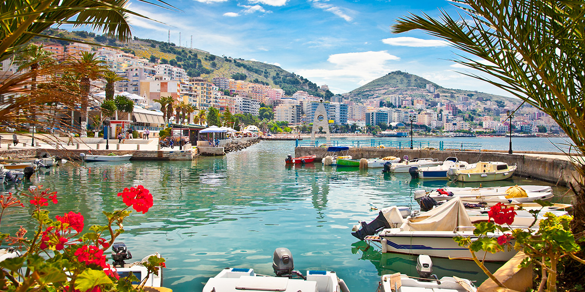 Havna i Saranda med båter, blomstring og turkist vann