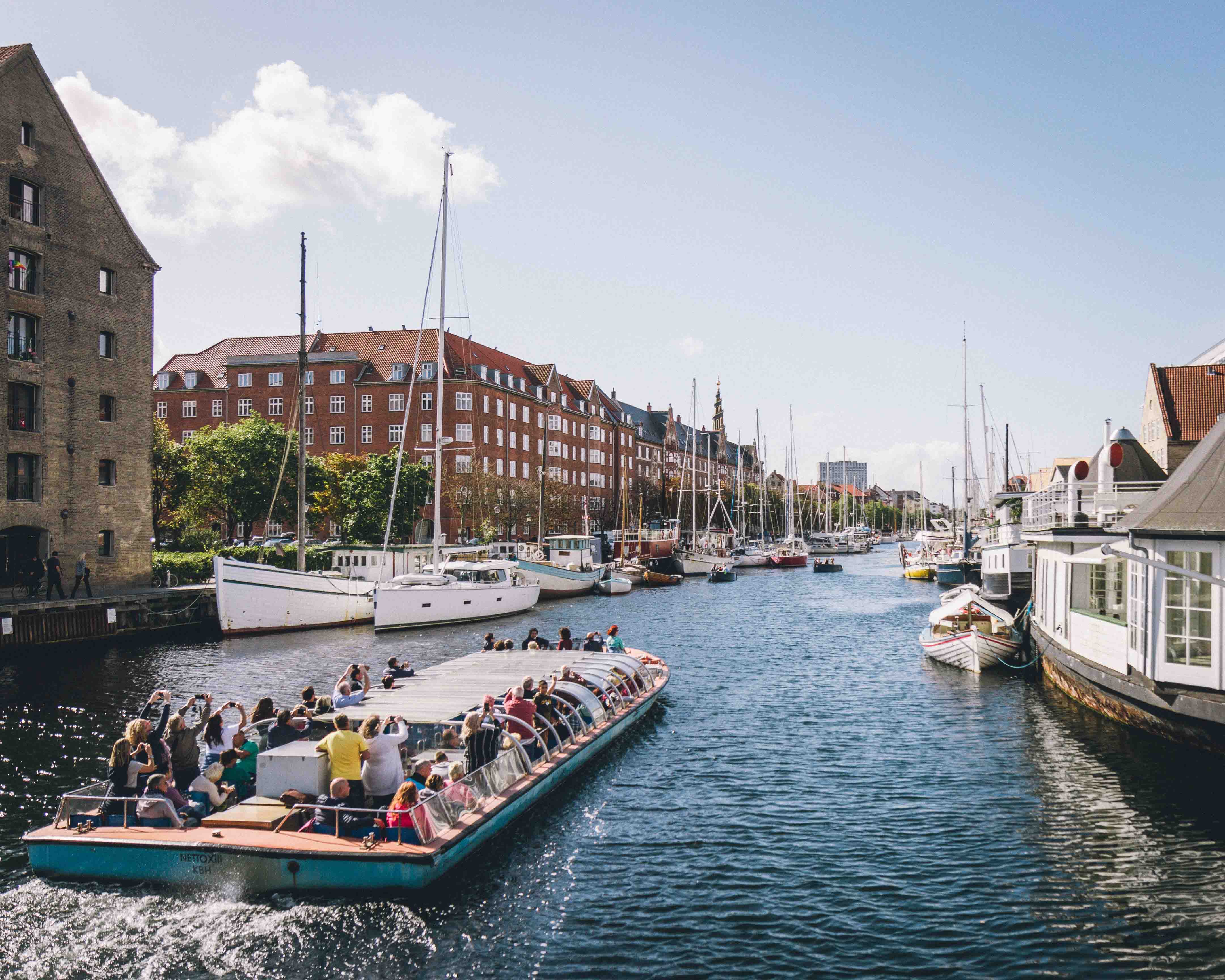 A canal boat with tourists raising their hands in the air and taking pictures. It's a sunny day.