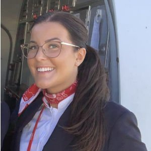 Airline crew with brown hair and glasses. smiling as she wears silk scarf around neck