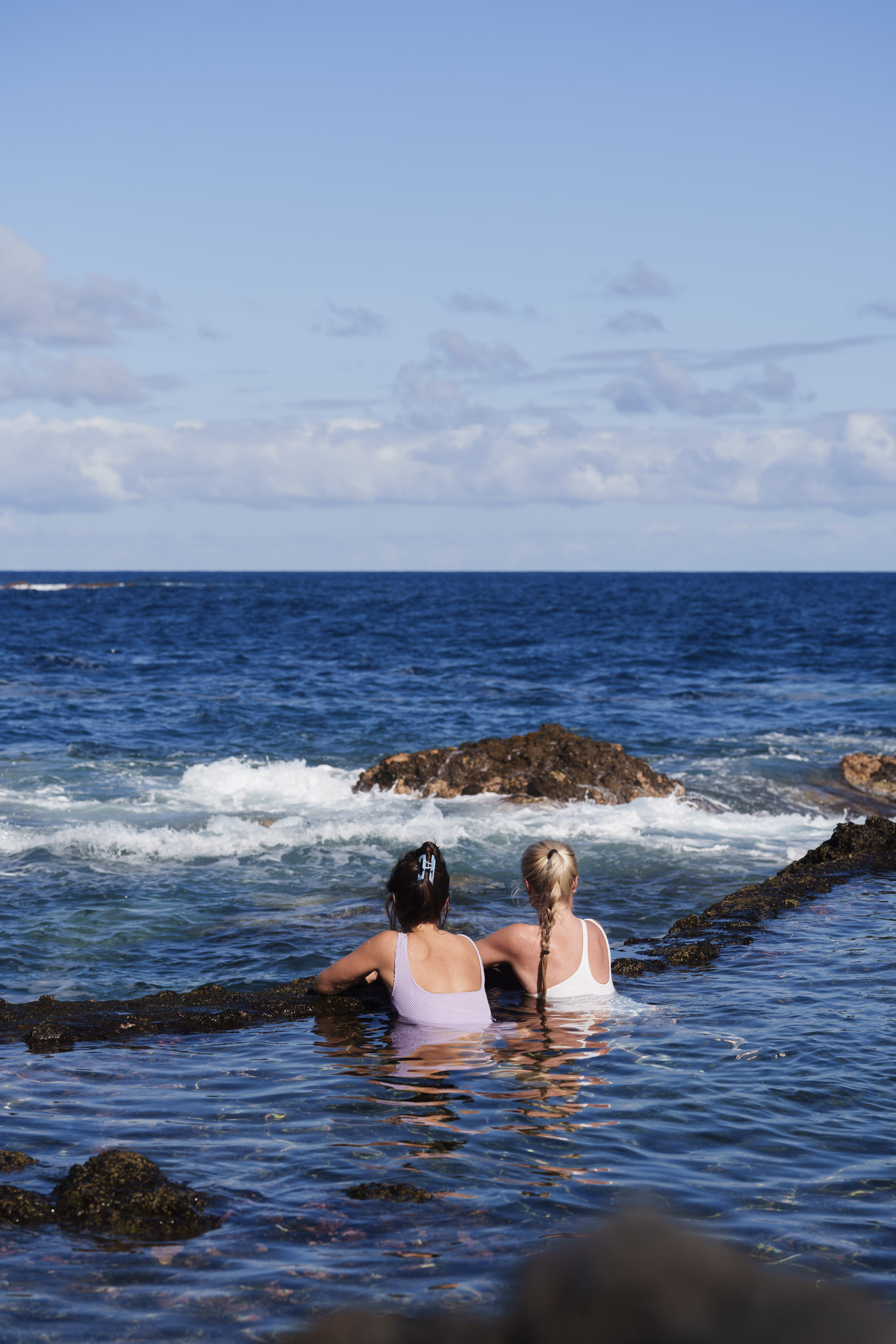 To kvinner ser utover havet i et naturlig  svømmebasseng