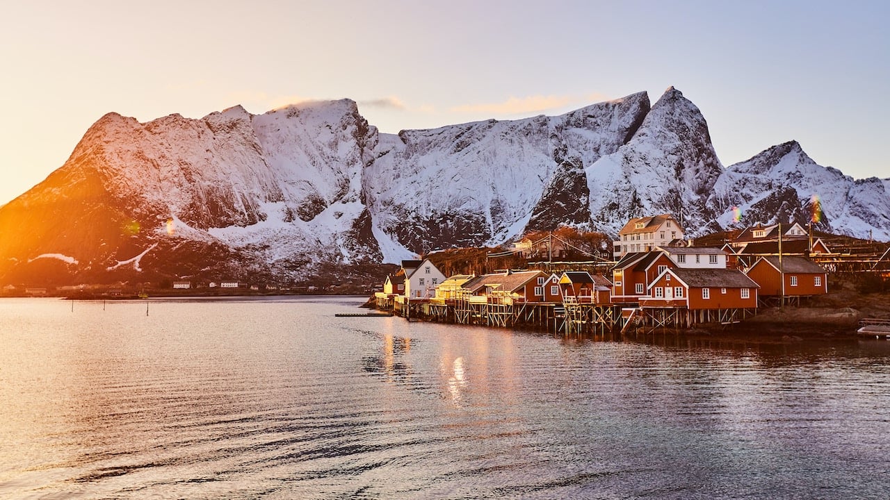 Solen går ned og kaster et orange lys over sneklædte bjerge og fiskerhytter