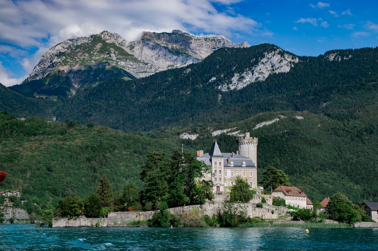 Et slot ved bredden af Annecy-søen med høje bjerge i baggrunden. 