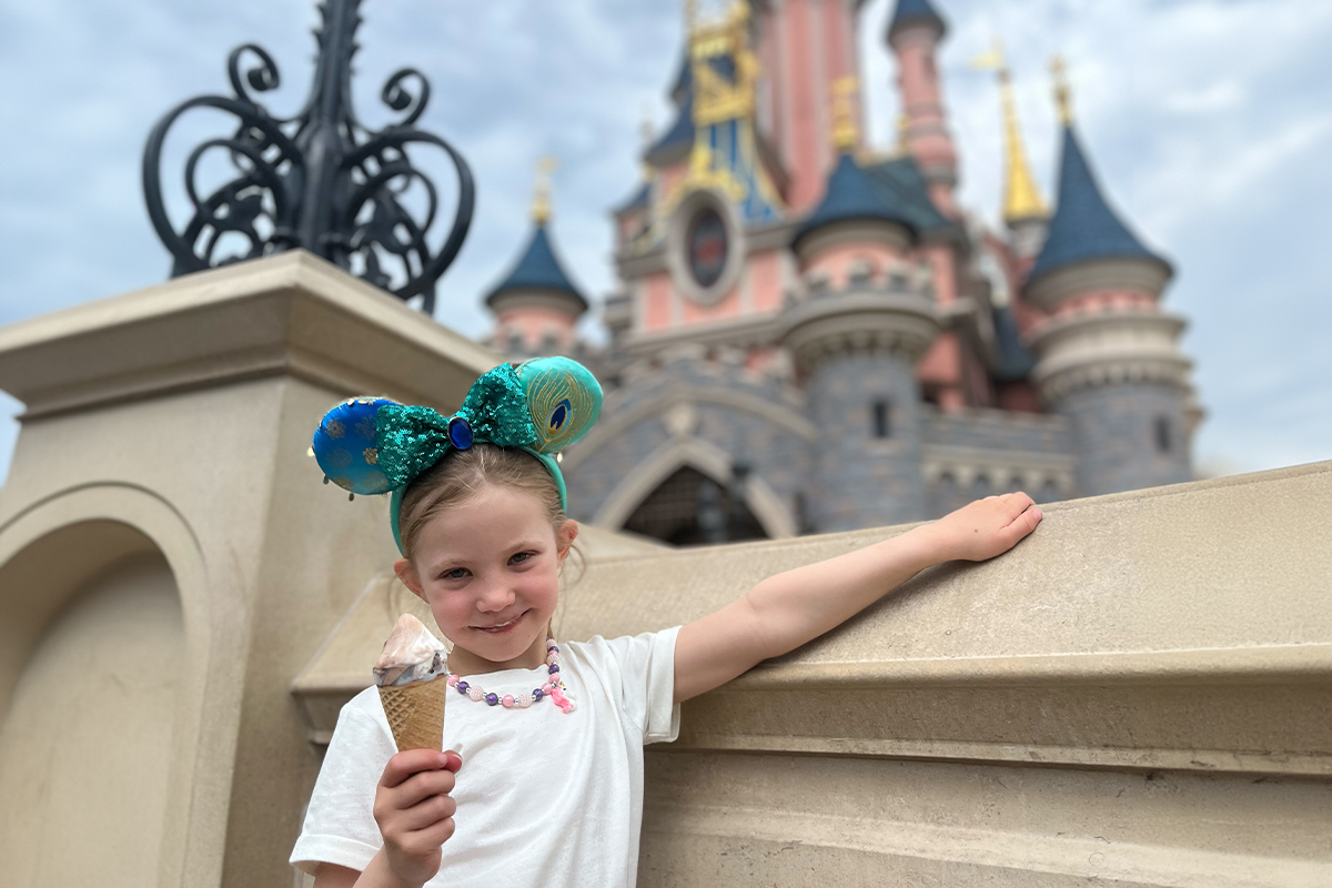 En jente står foran et rosa slott i Disneyland