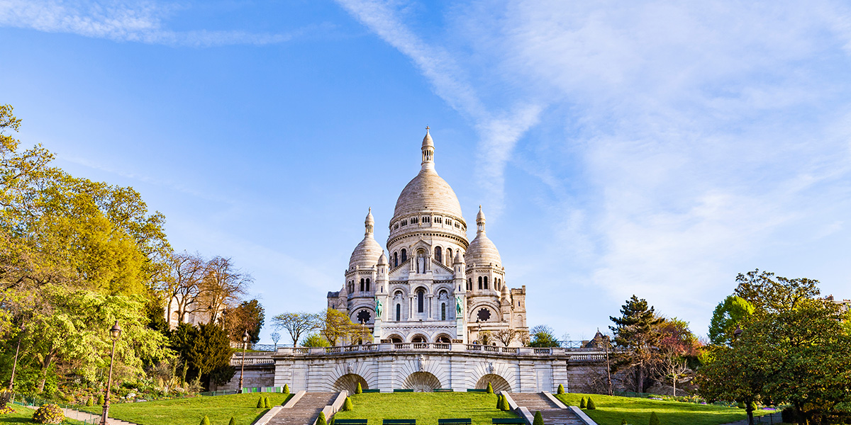 Sacré-Coeur-basilikaen sett litt nedenifra med blå himmel og frodig natur rundt.