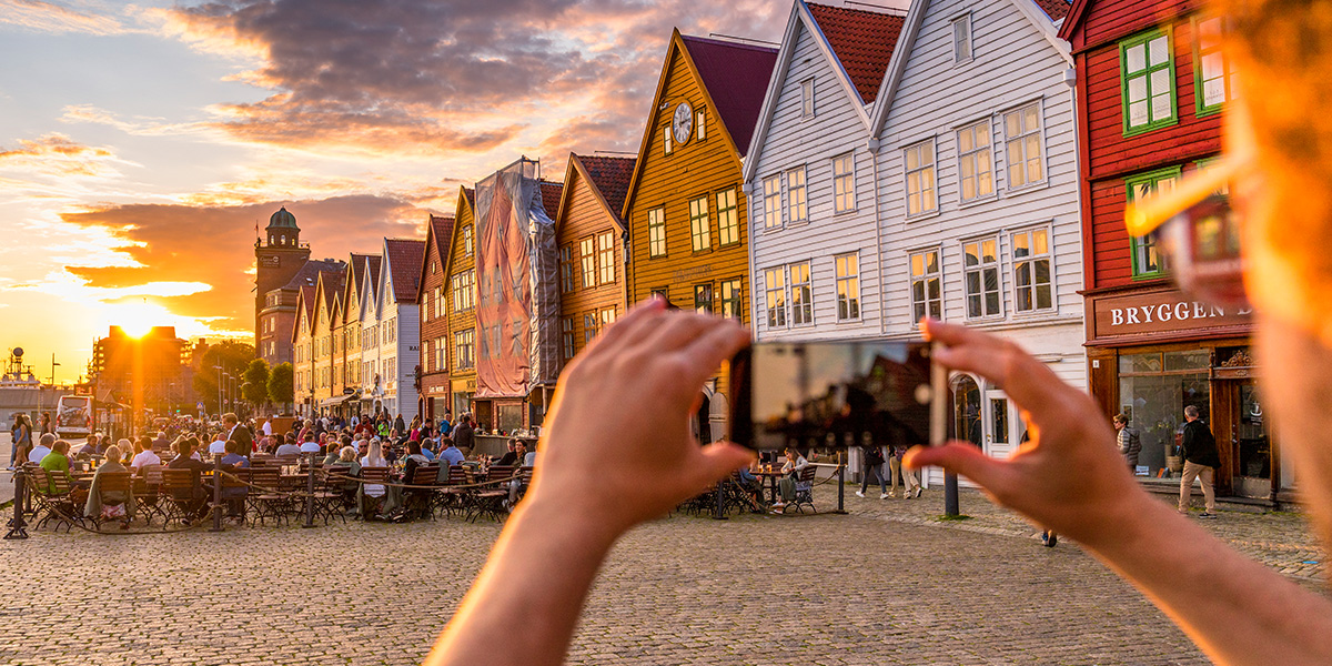 Person taking a photo of Bergen Harbour on their smartphoneTake in the charm at the famous Bryggen harbour in Bergen. Photo: © Getty Images