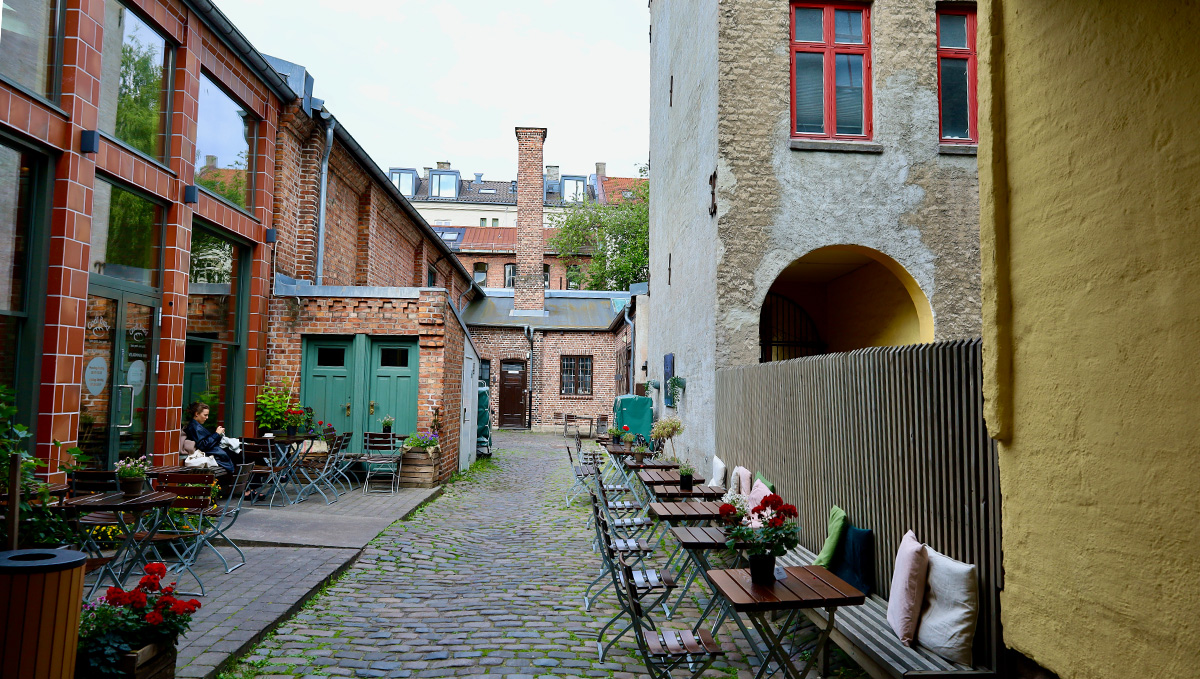 A photo of a backyard with benches along the wall. Opposite is a brick building.