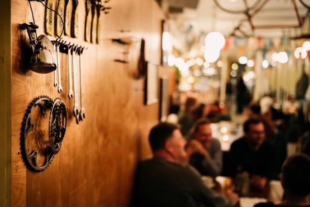 The interior of the Peloton. There is cycle gear hanging on the wood-panelled walls. In the background, people are sitting engaged in pleasant conversation. There is a cosy atmosphere.