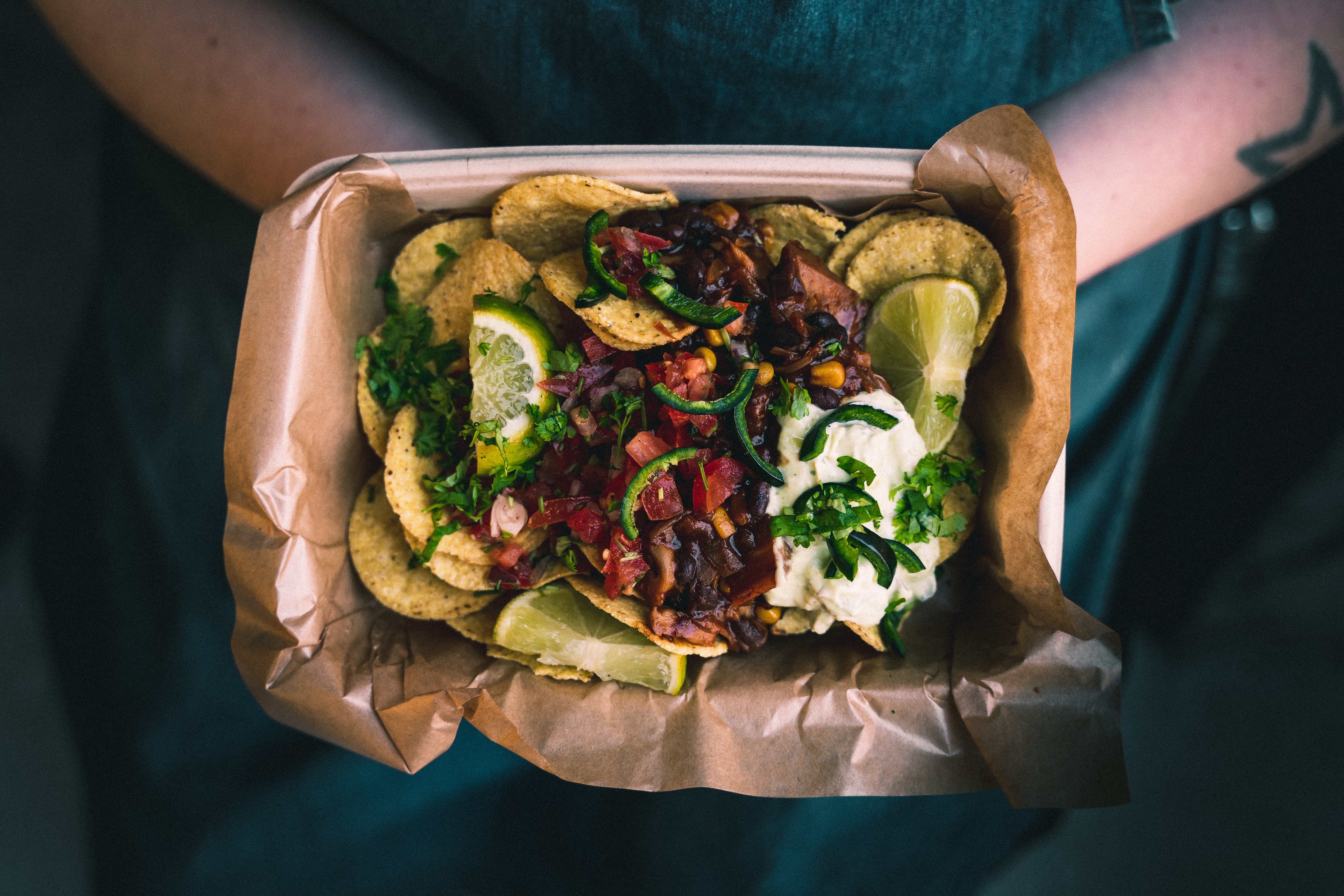 Two hands holding a bowl with nachos and chili con carne.
