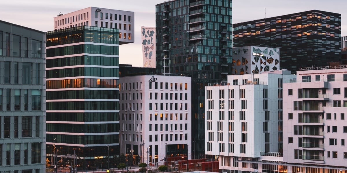 A photo of modern buildings in Oslo illuminated by the warm glow of the sunset. The buildings are white with hints of glassy green.
