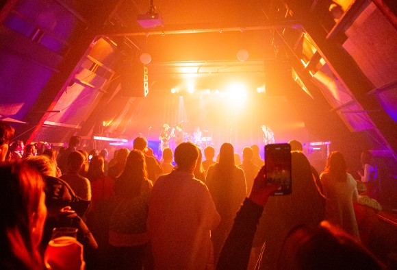 A concert with pink and yellow lighting. The floor is yellow from the young people dancing on it. The atmosphere is good.