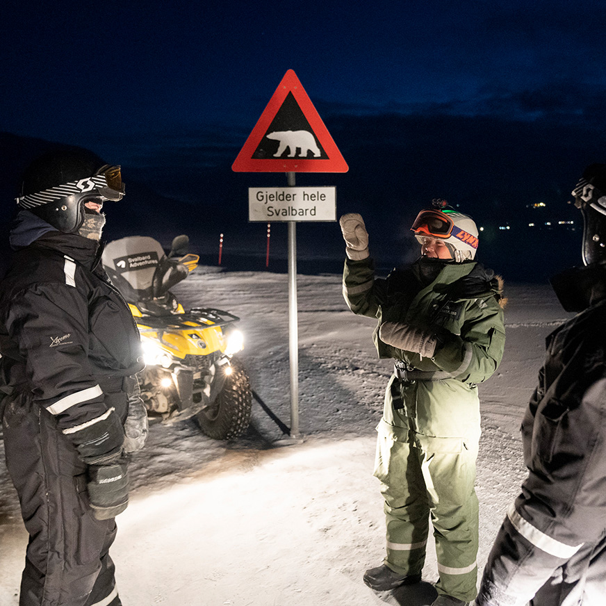 Noen mennesker står i termodress i mørket foran et isbjørnskilt