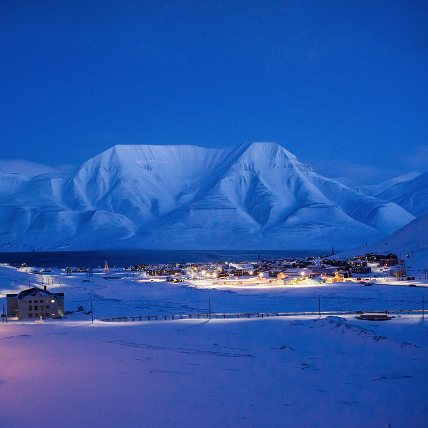 Et iskledd landskap med fjell og lys fra en liten by i blåtimen
