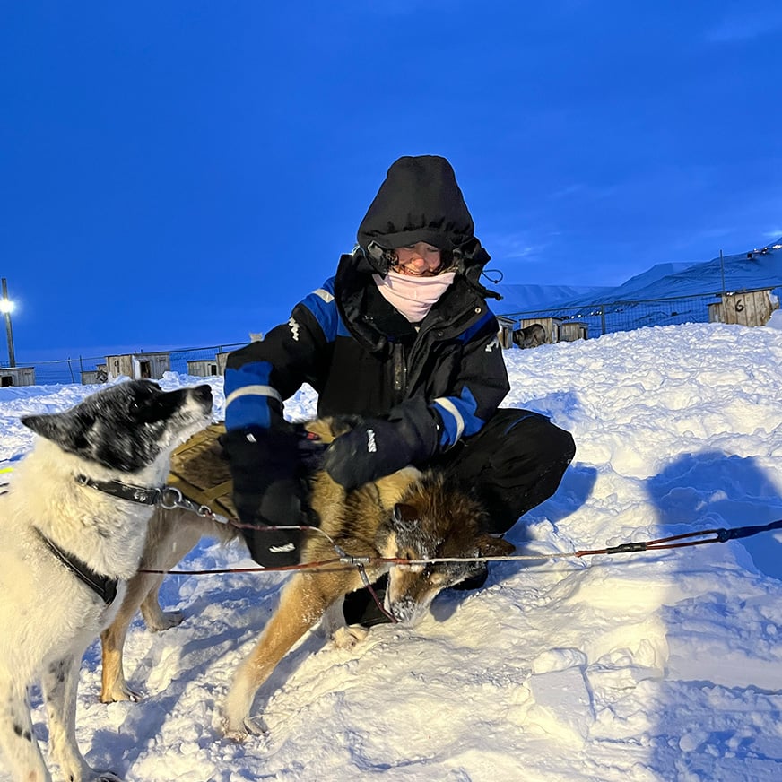 En kvinne i termodress koser med en husky i et snøkledd landskap