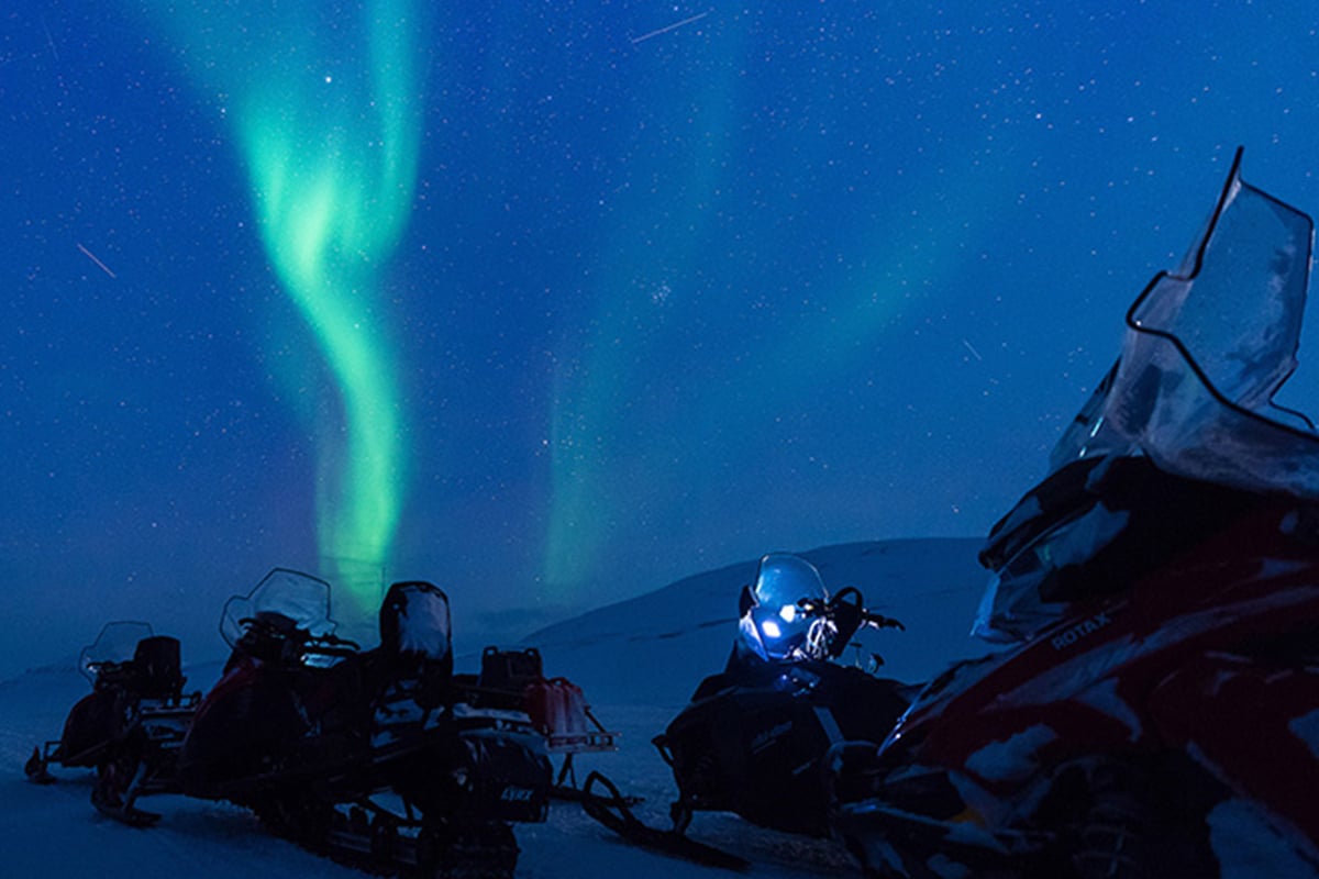 Nordlys over snøscootere i mørket