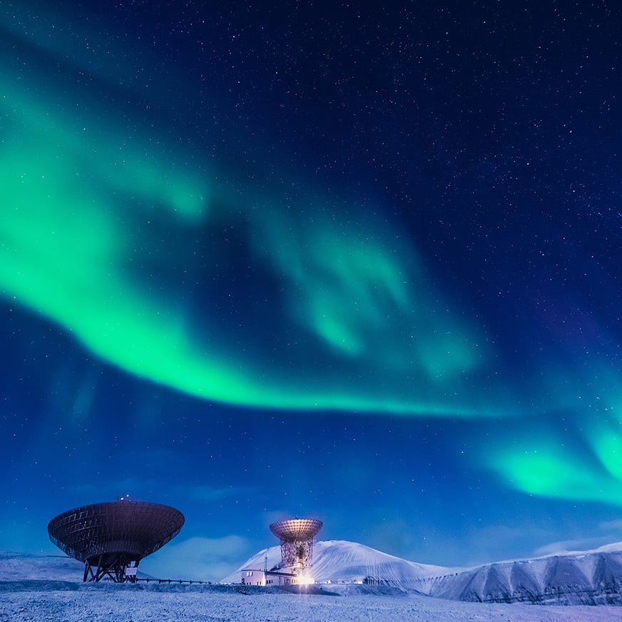 En satellitt plassert i et isdekket landskap med en nordlyshimmel over seg.