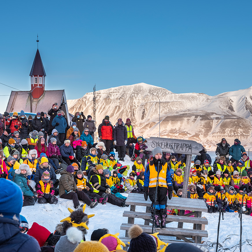 En samling av mennesker foran en kirke med fjell i bakgrunnen