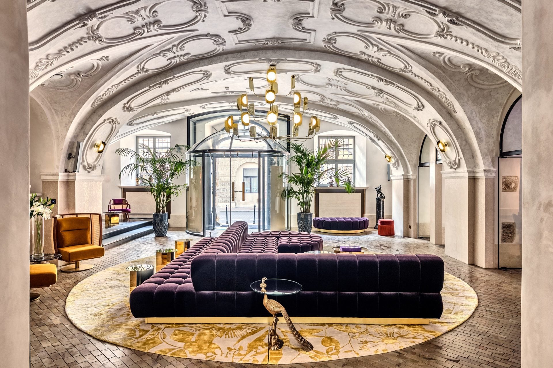 Hotellobby med böjt vitt tak, stor guldfärgad taklampa och mörklila designsoffa