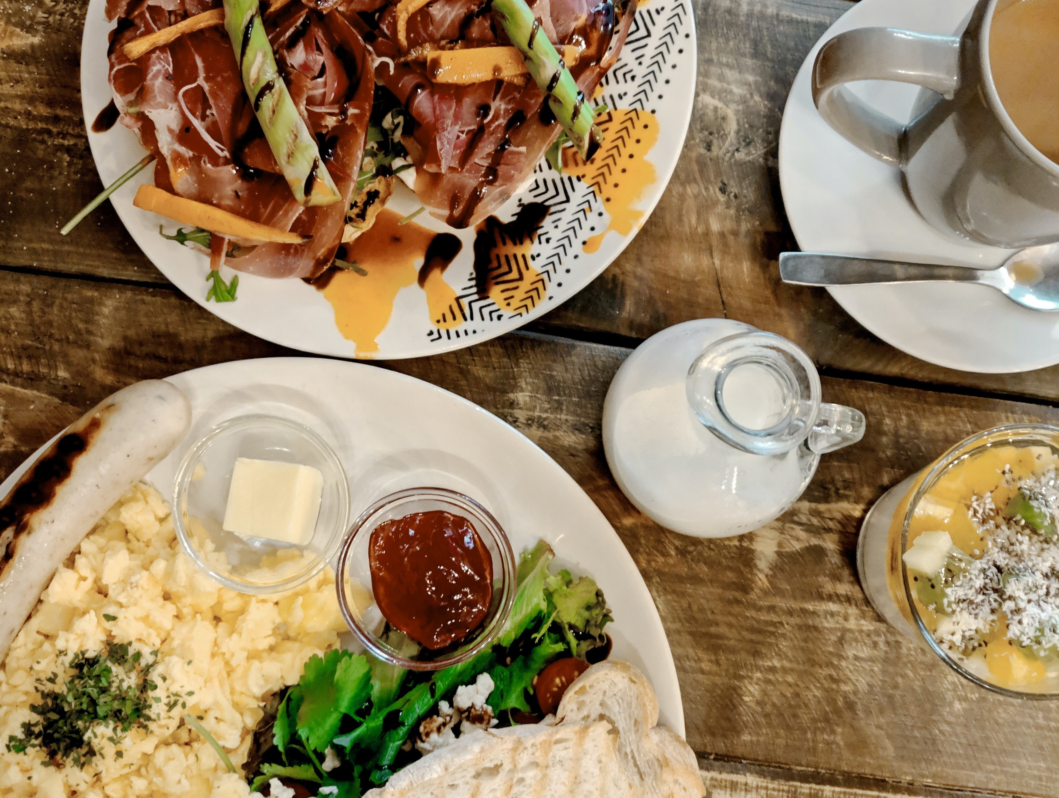 Billede af mad på et rustikt træbord. Asparges og spegeskinke med balsamico-reduktion. Broccoli og omelet på en anden tallerken.