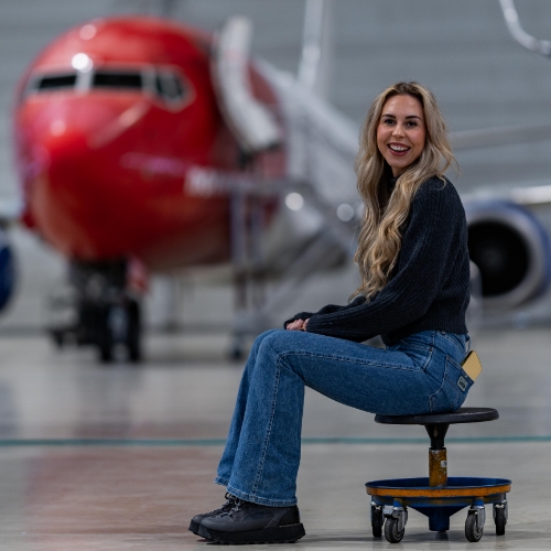 Woman sitting on a stool before a large airplane