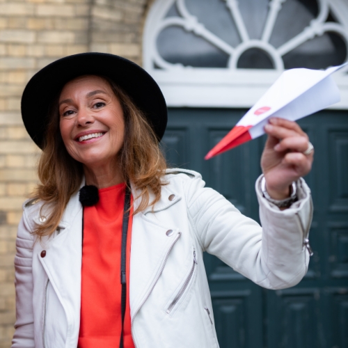 Woman with hat and red dress holding up a paper aeroplane